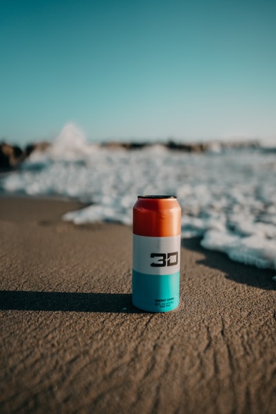 白天海浪附近棕色沙滩上的橙色和白色塑料瓶